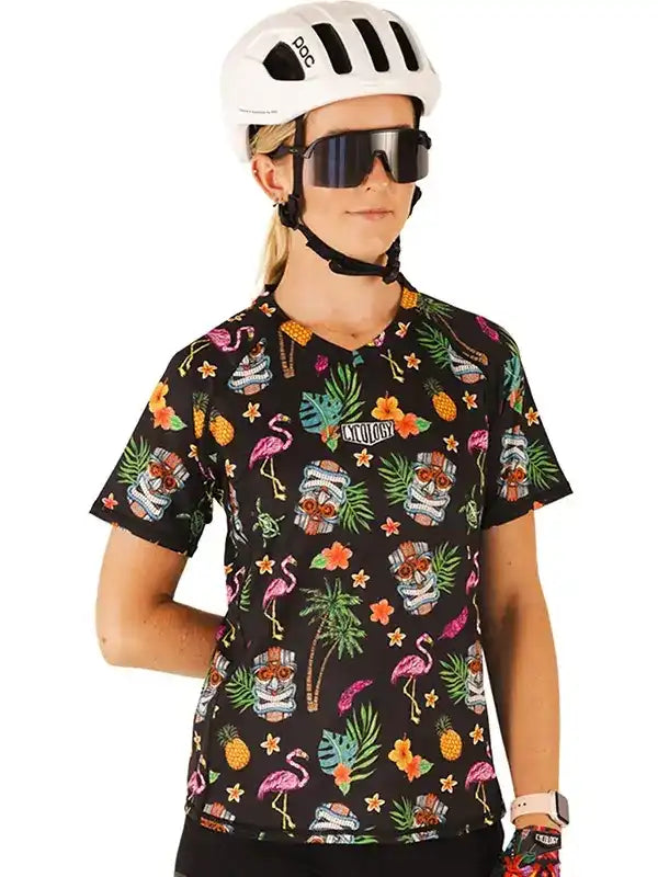 Woman wearing tropical print cycling jersey with flamingos, pineapples, and tiki masks, paired with helmet and sunglasses