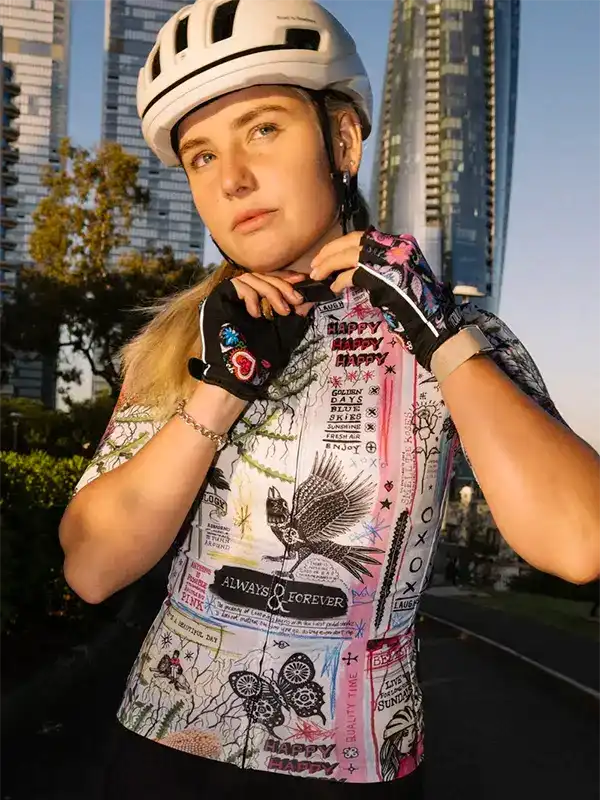 Woman in colorful cycling jersey with bird and butterfly print, wearing helmet, urban backdrop