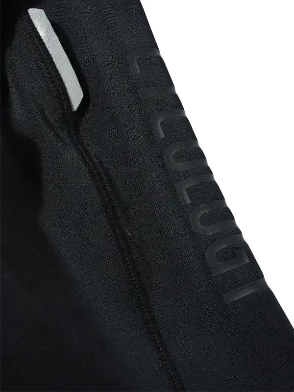 Close-up of a black Cycling bib leg with a large tonal vertical 'CYCLOLOGY' logo on the side and a small white reflective strip near the top.