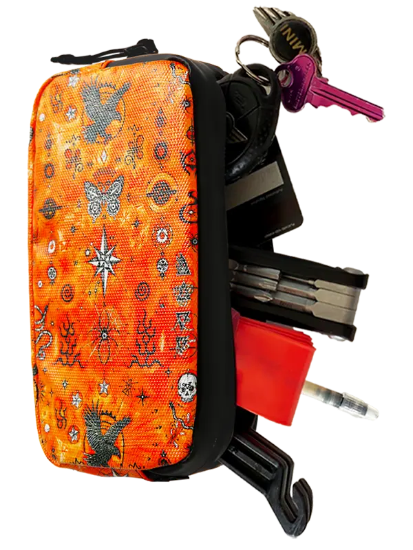 An orange tactical first aid kit pouch with a black border and occult-themed pattern, shown with keys, a multi-tool, a red emergency whistle, and other survival tools pulled out from the side against a white background.