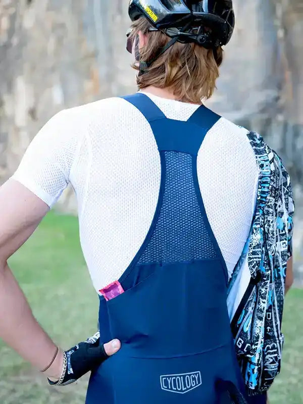 Man wearing blue cycling bib shorts with mesh back panel, white jersey, and helmet outdoors