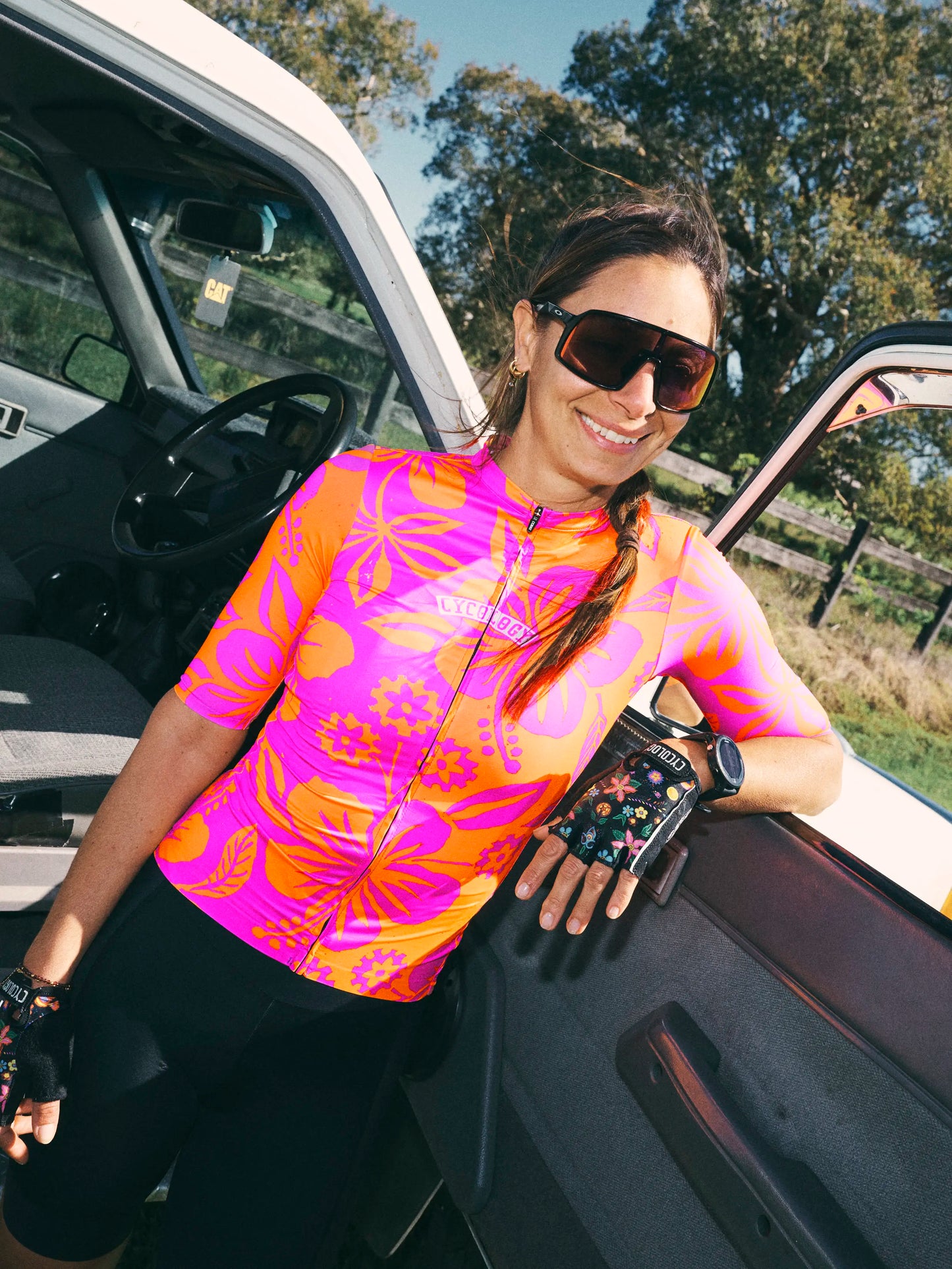 Woman in a colorful cycling jersey standing next to a vehicle outdoors
