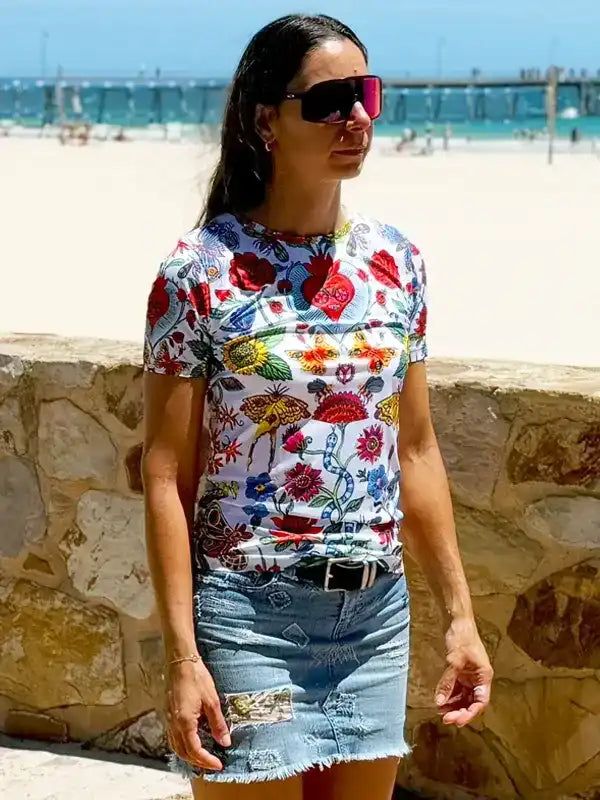 Woman wearing colorful floral print t-shirt with denim skirt at beach, stylish casual summer outfit