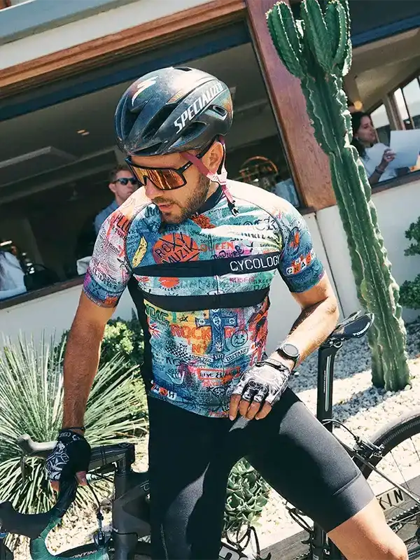 Man in colorful graphic cycling jersey and black shorts, wearing Specialized helmet, outdoors near cactus