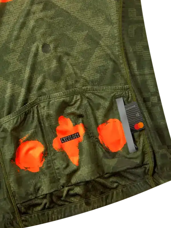Olive green cycling jersey with orange graphic design and rear storage pockets for ride essentials.