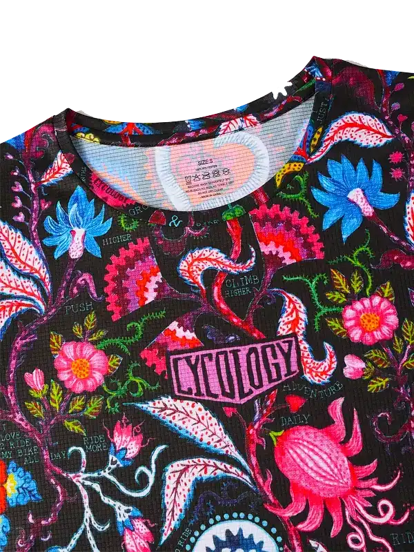 Vibrant floral cycling jersey with bold pink, blue, and red patterns on black fabric, featuring 'CYCOLOGY' logo and motivational phrases.
