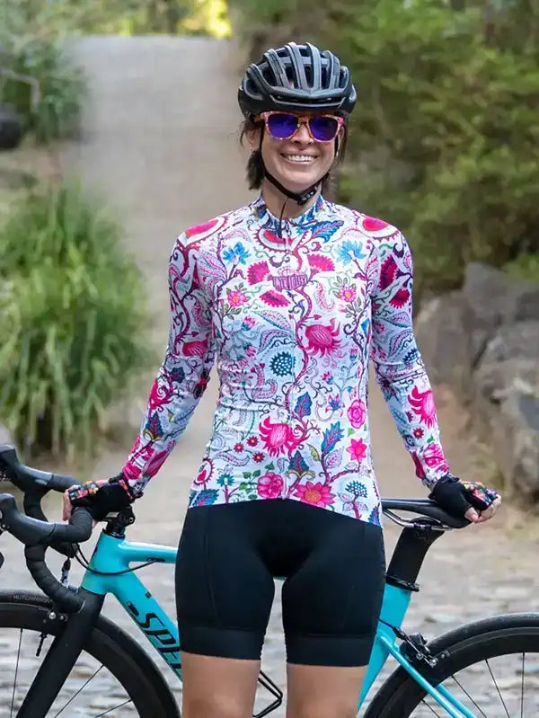 Woman in colorful floral cycling jersey and black shorts, smiling with bike outdoors