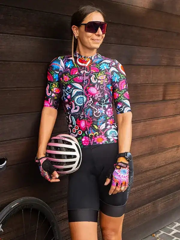 Woman in colorful floral cycling jersey and black shorts holding helmet, ready for ride
