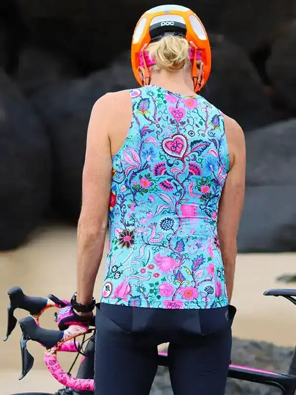 Woman in colorful floral cycling jersey and orange helmet, holding bike outdoors