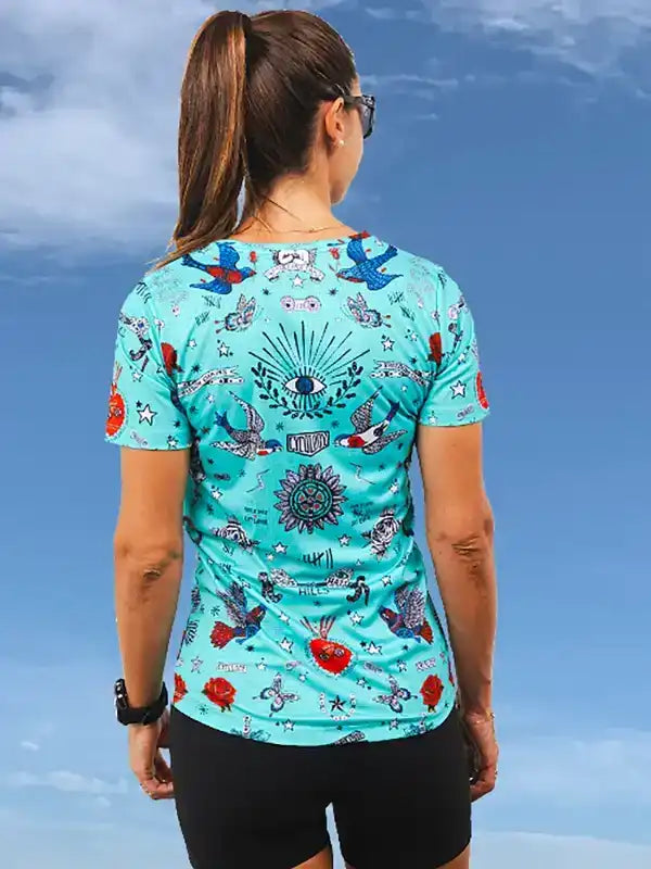 Women's cycling jersey with vibrant tattoo-style print, featuring birds, stars, and eye motifs on teal fabric.