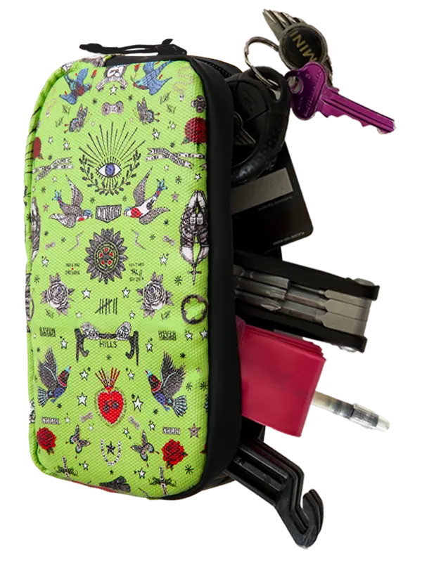 A bright lime green tactical pouch with a black zipper and black trim, decorated with a tattoo-style pattern featuring birds, roses, and religious symbols. The pouch is shown loaded with various accessories including keys, a pink wallet, a black cardholder, and a pen, all isolated on a white background.