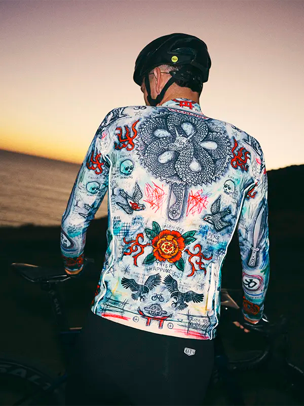 Person wearing a colorful cycling long sleeve jersey  with intricate designs against a sunset background