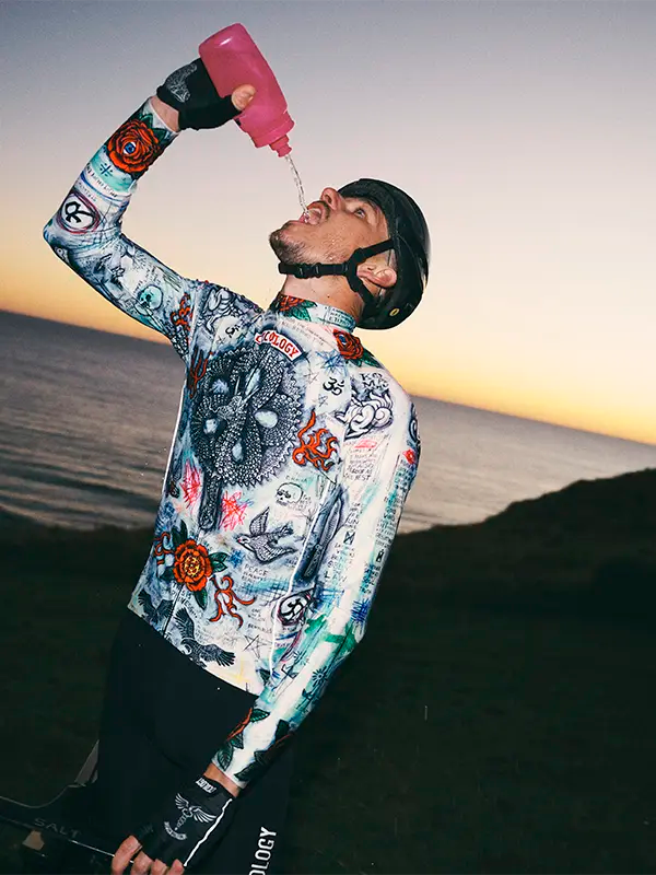 Person wearing a colorful cycling long sleeve jersey with intricate designs against a sunset background