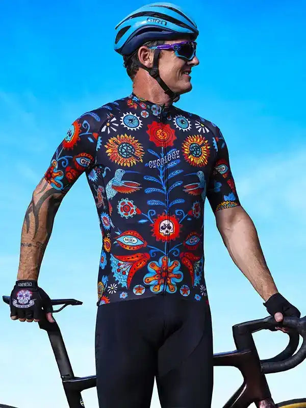 Men's cycling jersey with vibrant floral and skull print, paired with black shorts and helmet for road biking.