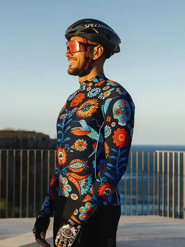 Man in vibrant floral and skull cycling jersey, helmet, and sunglasses, coastal view background