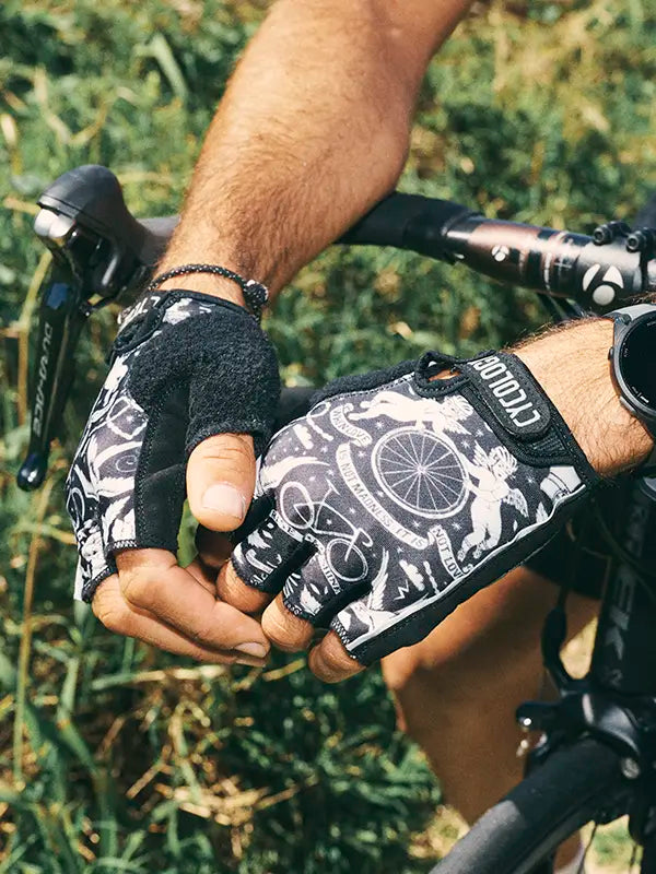 Close-up of a person wearing black and white cycling gloves with a bicycle design, holding onto a bike handlebar.