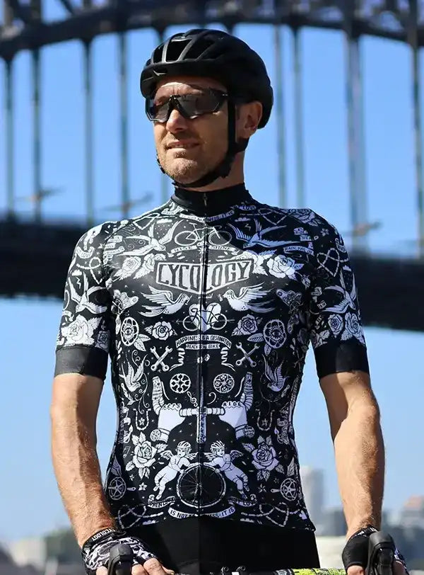 Man wearing black and white tattoo-style cycling jersey with helmet, outdoors near bridge