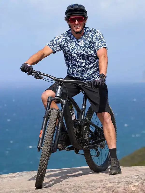 Man cycling in floral jersey and black shorts on mountain bike near ocean