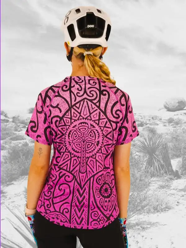 Woman wearing pink patterned cycling jersey with black designs, white helmet, outdoors