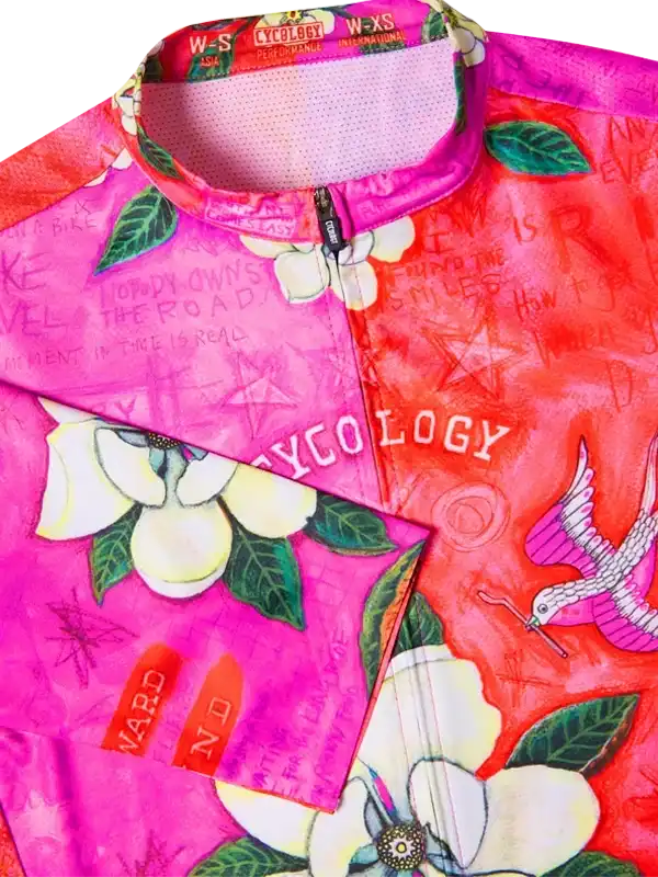 Vibrant floral cycling jersey with bold pink and red hues, featuring white flowers and bird designs.