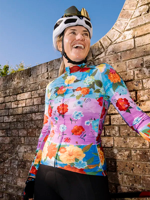 Person wearing a colorful floral cycling jersey and helmet against a stone wall.