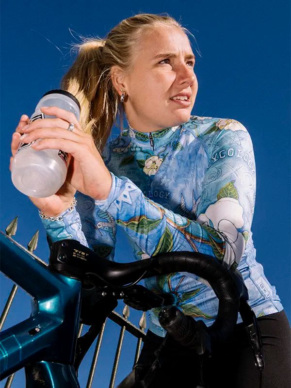 Woman in a blue cycling jersey holding a water bottle against a blue background