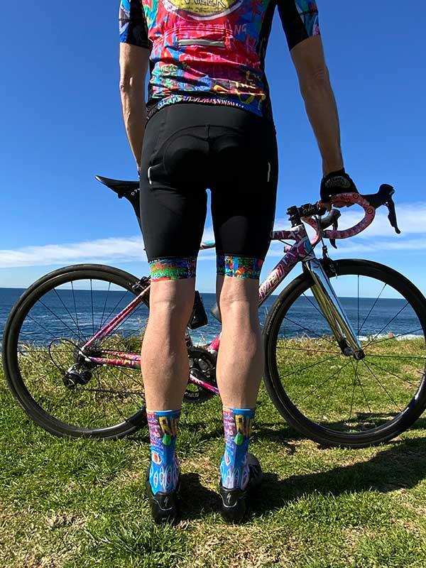 Cyclist in colorful cycling jersey and matching socks standing with road bike by ocean
