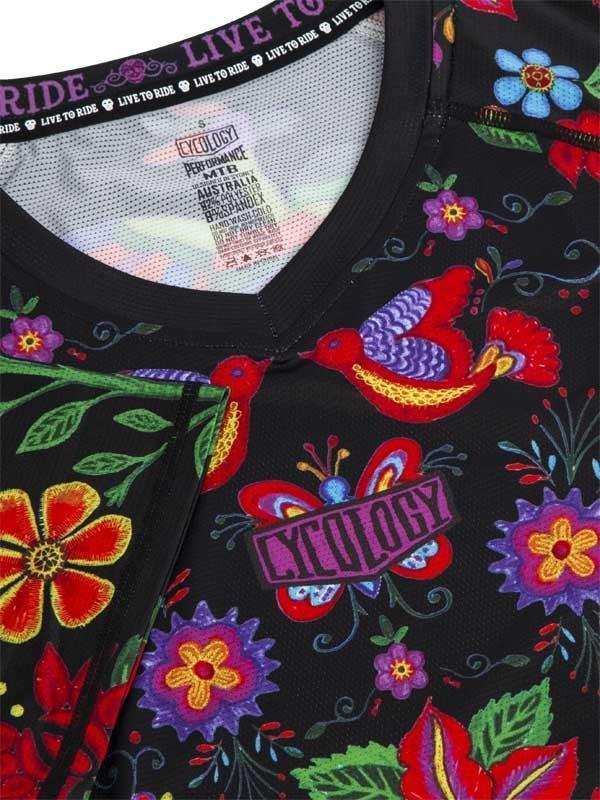 Black cycling jersey with colorful floral and bird print, featuring 'Live to Ride' tag and performance fabric label