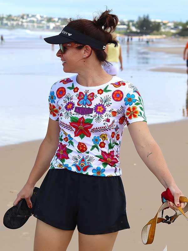 Woman in colorful floral cycling jersey and black shorts at beach, wearing visor and sunglasses
