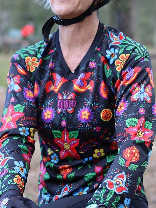 Woman wearing vibrant floral cycling jersey with colorful bird and flower patterns, ideal for road or trail rides.