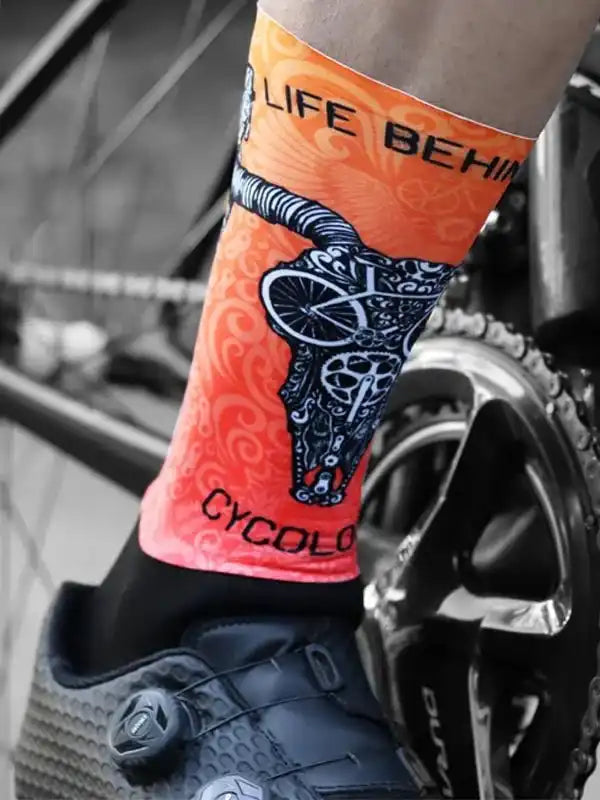 Vibrant orange cycling sock with skull & bike design, worn with clip-in shoe near bike crank