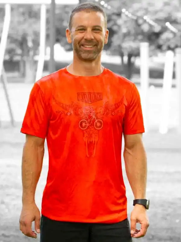 Man wearing vibrant orange cycling t-shirt with skull and bike graphic, ideal for men's cycling apparel
