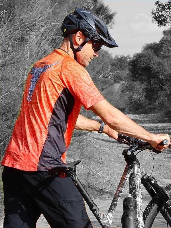 Man cycling in vibrant orange and black jersey with graphic design, wearing helmet on trail