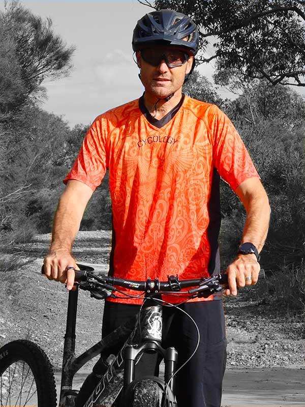 Man in orange patterned cycling jersey riding mountain bike outdoors