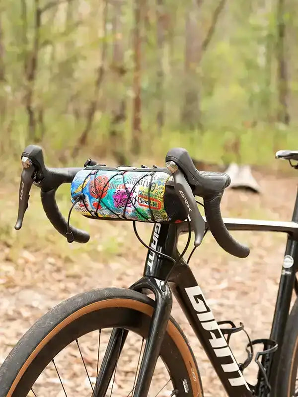Colorful cycling handlebar bag on road bike in forest trail, ideal for bikepacking and commuting.