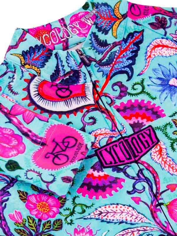Vibrant floral cycling jersey with bold pink, blue, and purple patterns, featuring bike motifs and brand tag details.