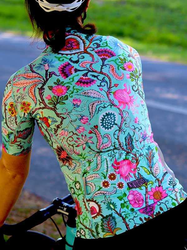 Woman cycling in vibrant floral jersey, colorful botanical print on teal cycling top, outdoor ride