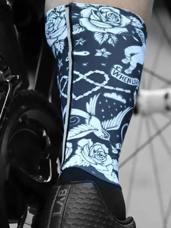 Cycling leg warmer with white rose and bird tattoo-style print on navy blue, worn with cycling shoe