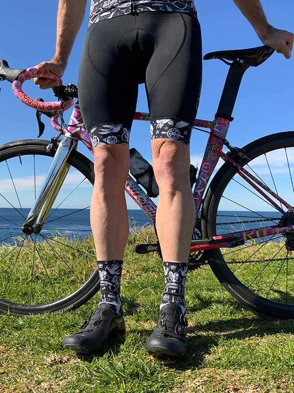 Men's cycling shorts and socks with graphic print, paired with road bike on grassy coastal trail