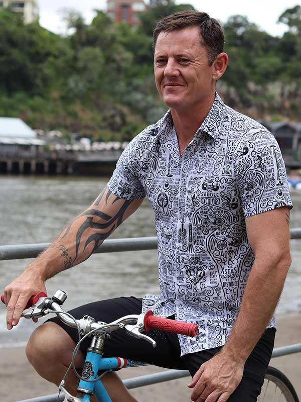 Man wearing graphic cycling shirt and shorts on blue bike by waterfront, ideal for casual rides